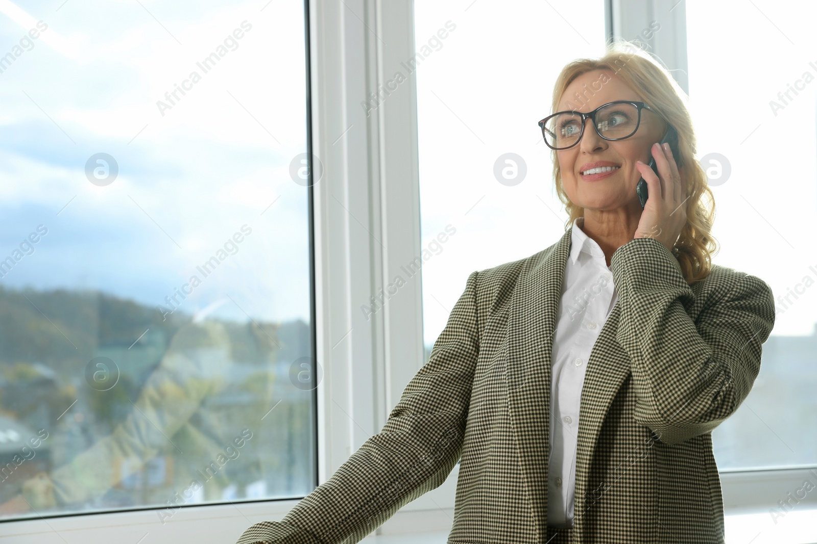 Photo of Lady boss talking on smartphone near window indoors, space for text. Successful businesswoman