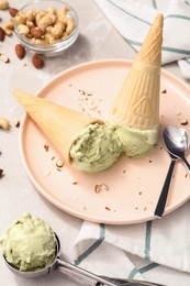 Photo of Delicious pistachio ice cream in wafer cones with chopped nuts served on light table