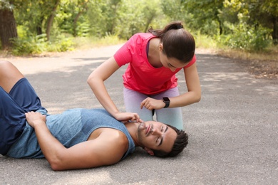 Photo of Young woman checking pulse of unconscious man in park. Space for text