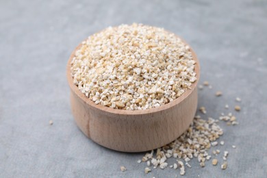 Photo of Raw barley groats in bowl on grey table, closeup