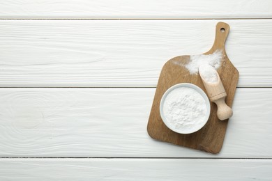 Baking powder in bowl and scoop on white wooden table, top view. Space for text