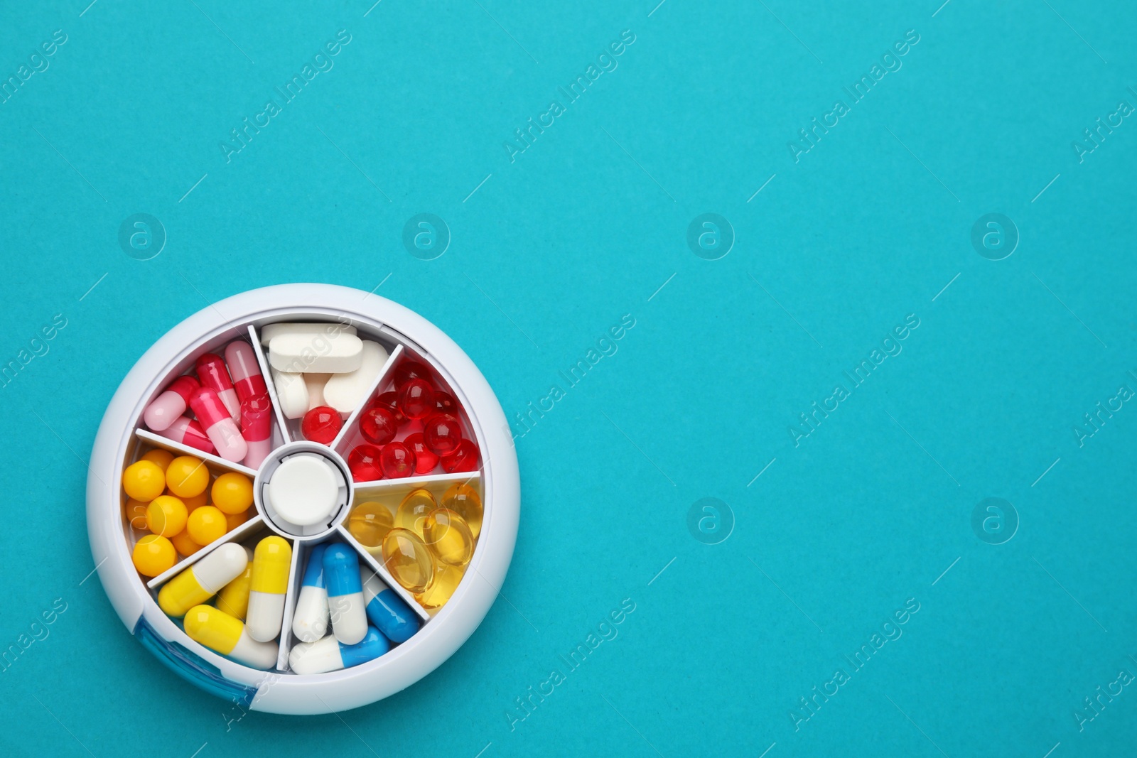 Photo of Plastic box with different pills on light blue background, top view. Space for text