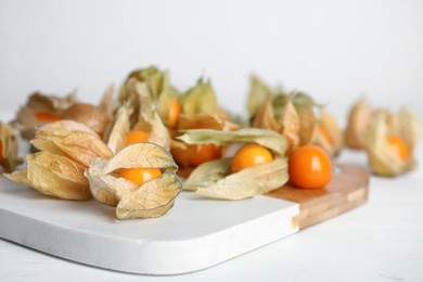 Photo of Ripe physalis fruits with dry husk on white wooden table. Space for text
