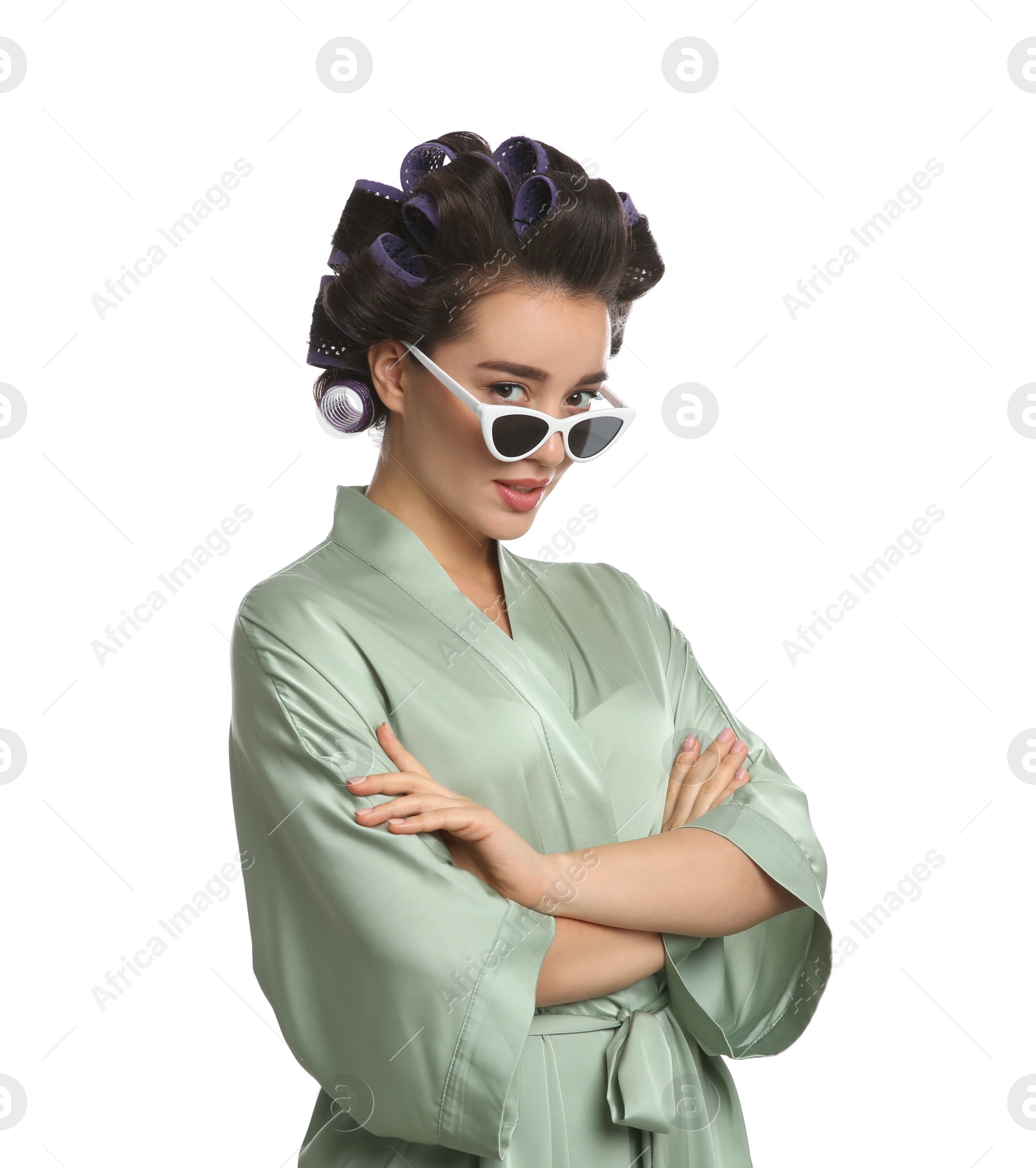 Photo of Happy young woman in silk bathrobe with hair curlers and sunglasses on white background