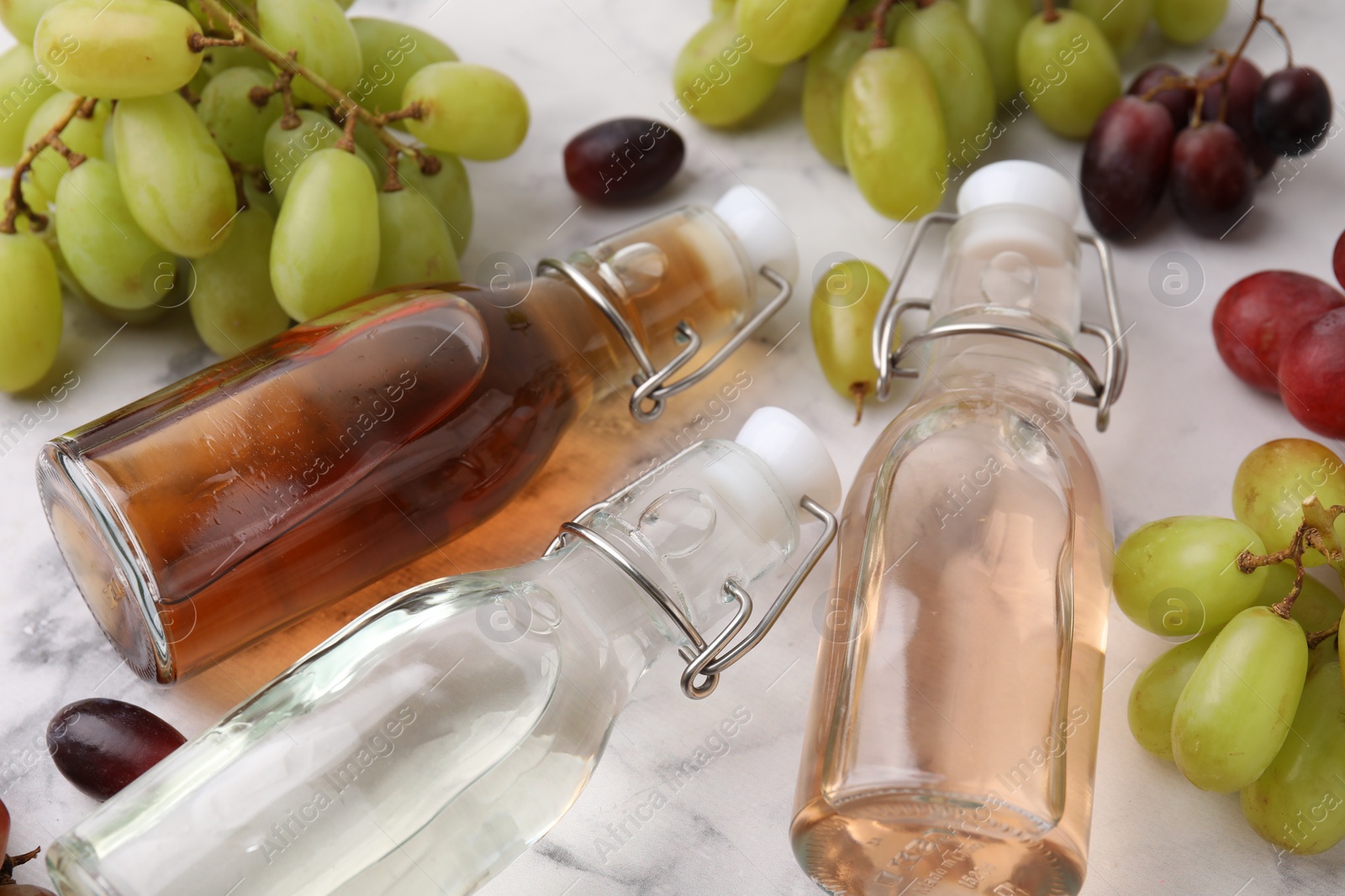 Photo of Different types of vinegar in bottles and grapes on light table, closeup