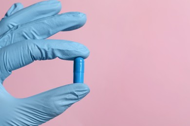 Doctor holding pill on pink background, closeup. Space for text