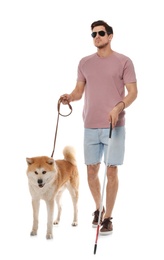 Photo of Blind man with walking stick and dog on leash against white background