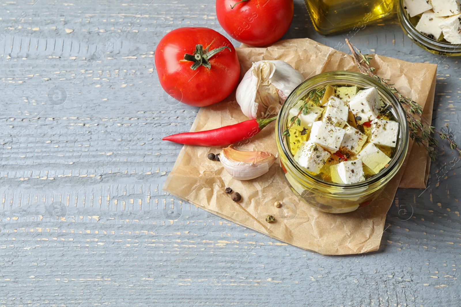 Photo of Composition with pickled feta cheese in jar on grey wooden table, above view. Space for text