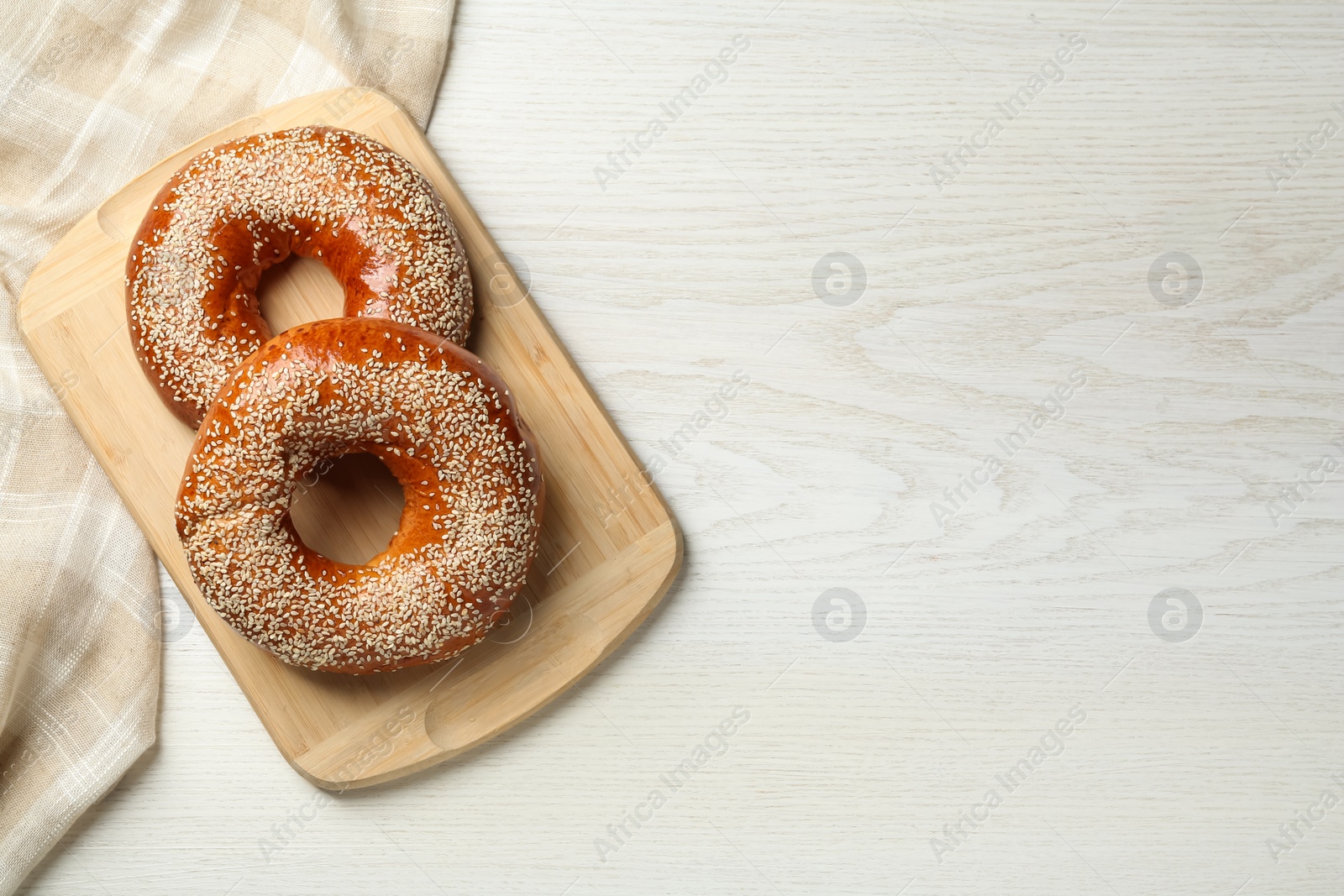 Photo of Delicious fresh bagels with sesame seeds on white wooden table, top view. Space for text