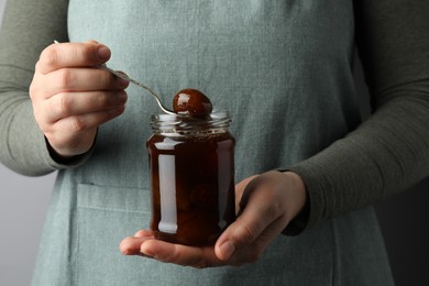 Photo of Woman holding jar of tasty sweet fig jam on grey background, closeup