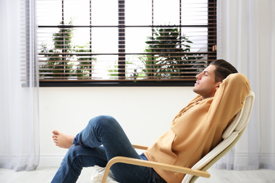 Photo of Attractive man relaxing in armchair near window at home