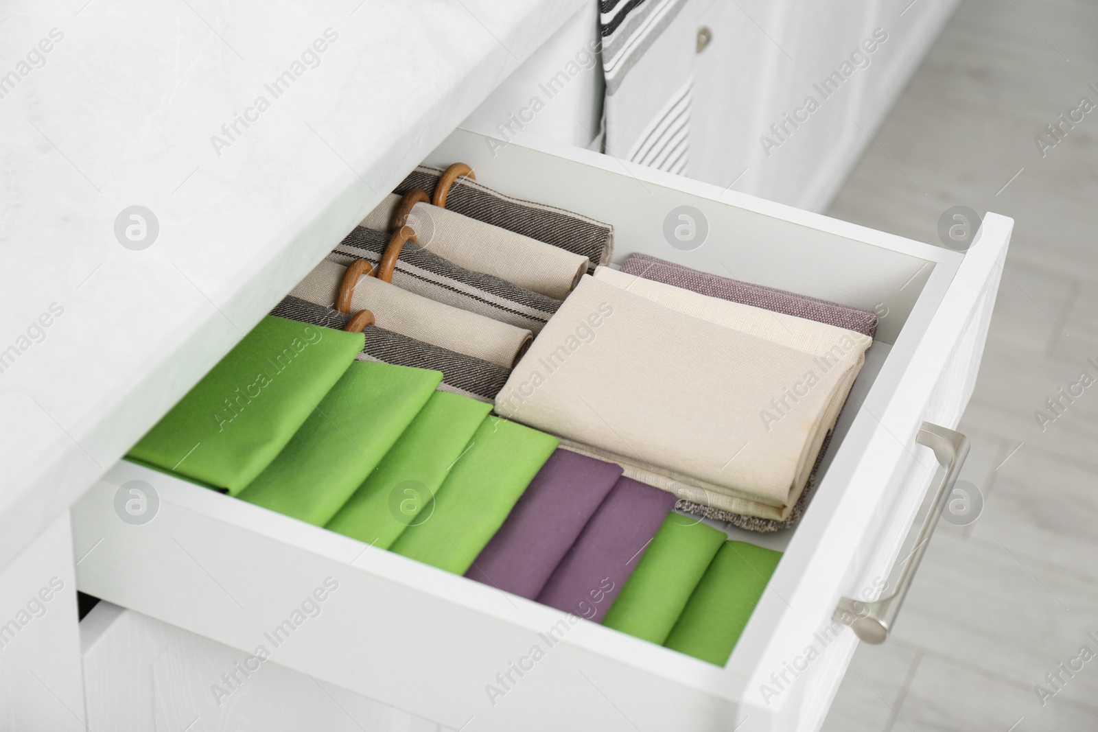 Photo of Open drawer with different folded towels and napkins in kitchen