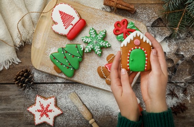 Photo of Woman holding delicious homemade Christmas cookie at wooden table, top view