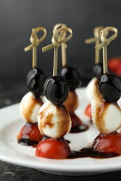 Photo of Tasty canapes with black olives, mozzarella and cherry tomatoes on dark textured table, closeup