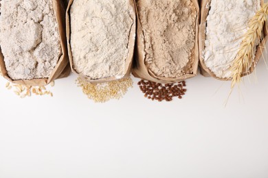 Paper bags with different types of flour on white background, top view. Space for text