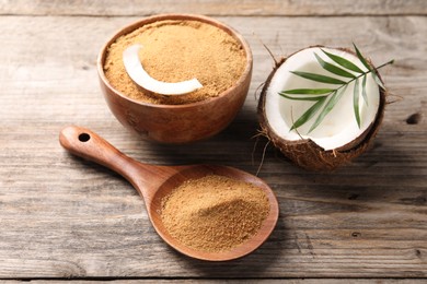 Coconut sugar in bowl, spoon, fruit and palm leaves on wooden table, closeup