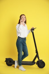 Photo of Happy woman with modern electric kick scooter talking on smartphone on yellow background