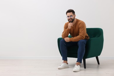 Photo of Handsome man sitting in armchair near white wall indoors, space for text