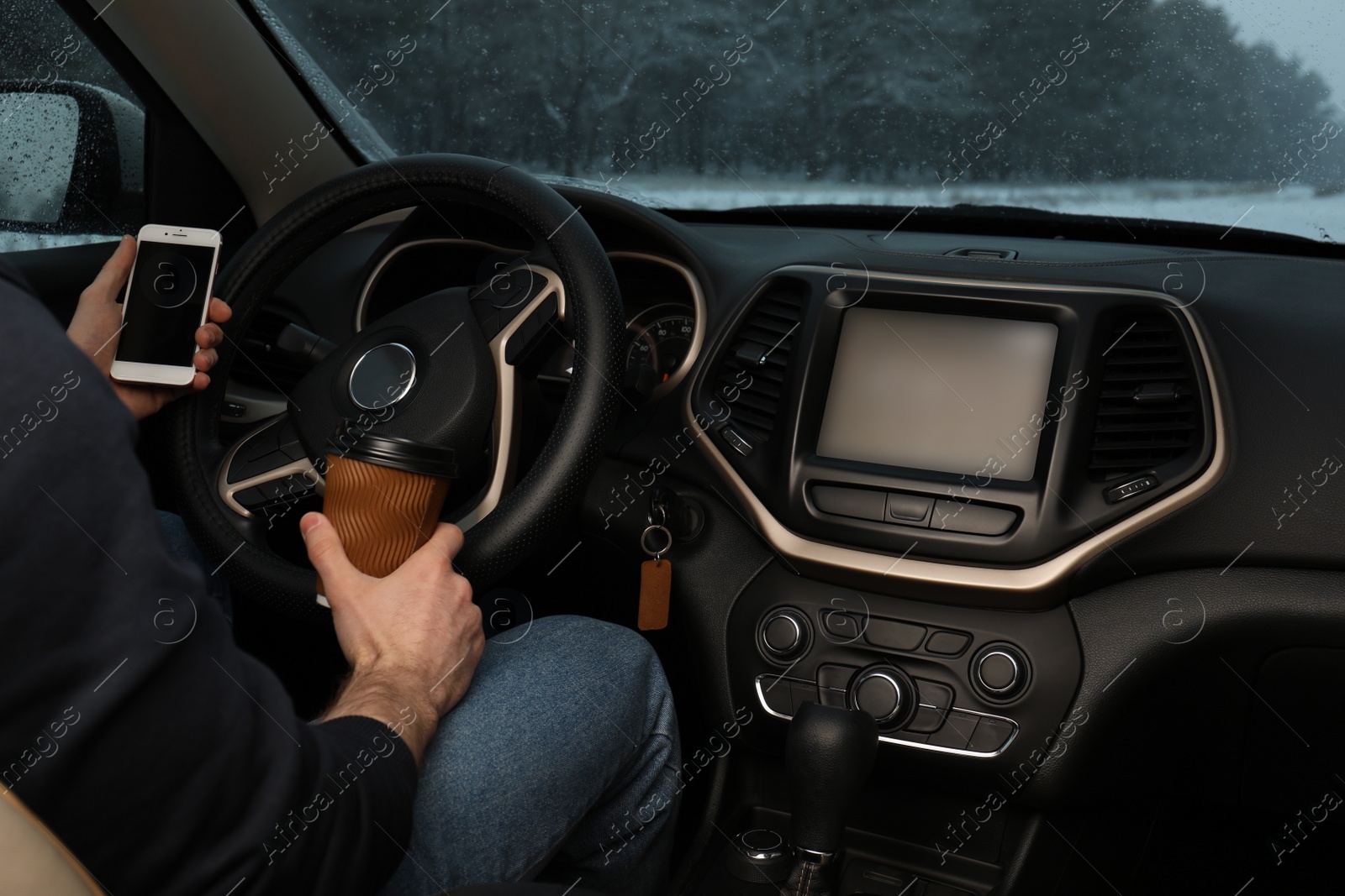 Photo of Young man with coffee and smartphone inside car, closeup