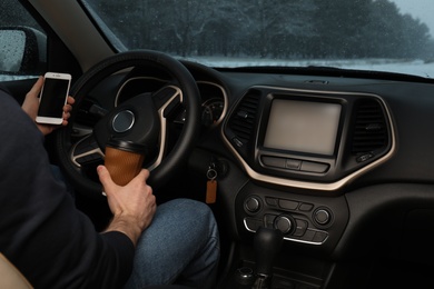 Young man with coffee and smartphone inside car, closeup