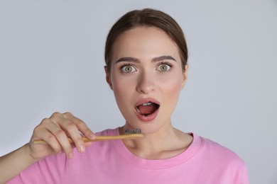 Photo of Surprised woman brushing teeth with charcoal toothpaste on light background