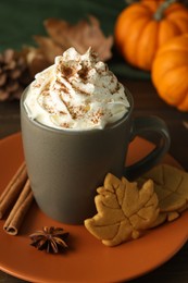 Photo of Tasty pumpkin spice latte with whipped cream in cup and cookies on table, closeup