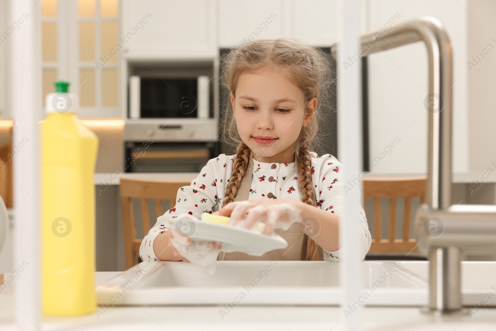 Photo of Little girl washing plate above sink in kitchen