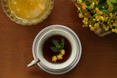 Photo of Cup of hot aromatic herbal tea, honey and linden blossoms on wooden table, flat lay