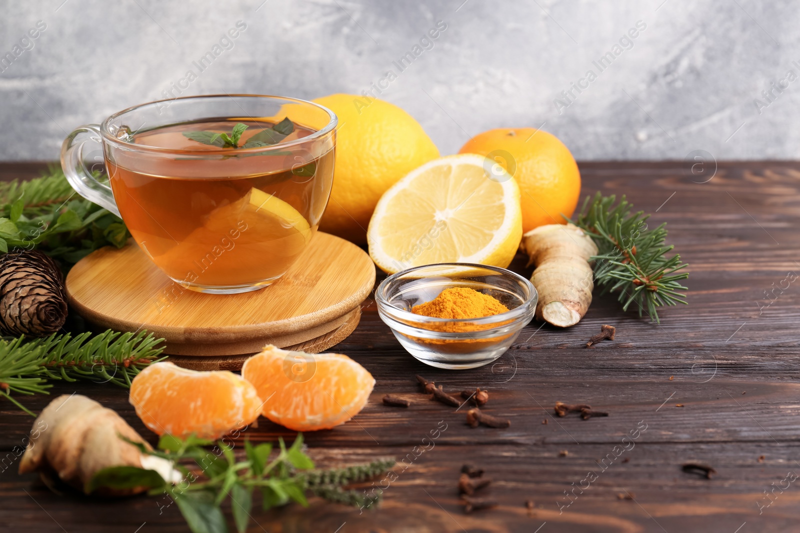 Photo of Glass cup of delicious immunity boosting tea and ingredients on wooden table. Space for text