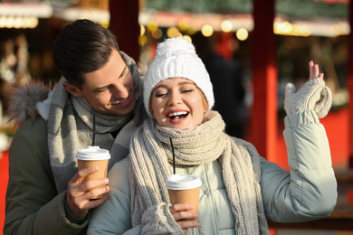 Photo of Happy couple in warm clothes with drinks at winter fair. Christmas season