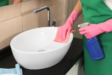 Woman in protective gloves cleaning bathroom sink with rag