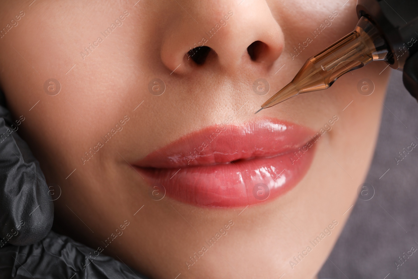 Photo of Young woman undergoing procedure of permanent lip makeup in tattoo salon, closeup