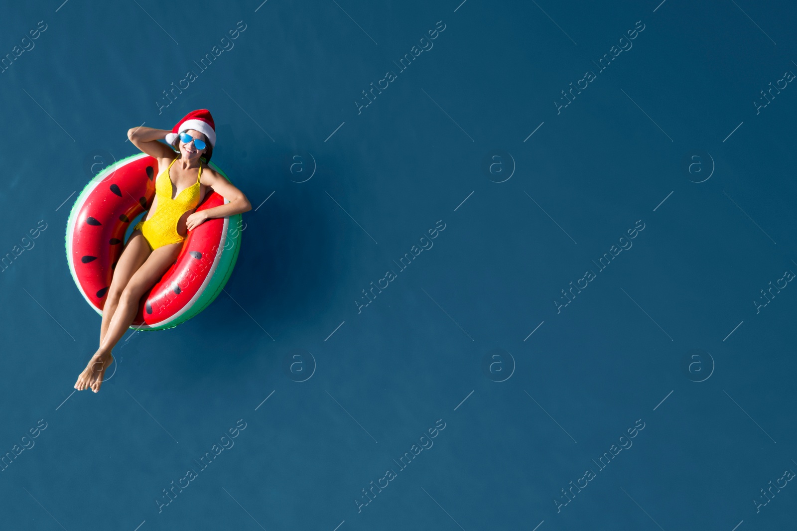 Image of Young woman wearing Santa hat and swimsuit with inflatable ring in sea, top view. Christmas vacation