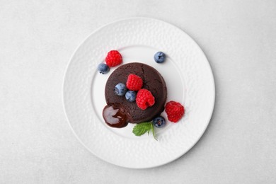 Plate with delicious chocolate fondant, berries and mint on light grey table, top view