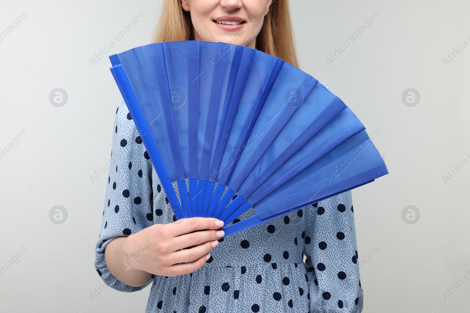 Photo of Woman with blue hand fan on light grey background, closeup