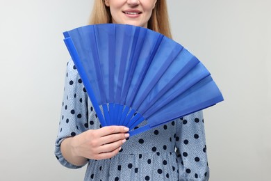 Photo of Woman with blue hand fan on light grey background, closeup