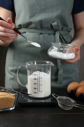 Photo of Woman adding baking powder into measuring cup at black wooden table, closeup