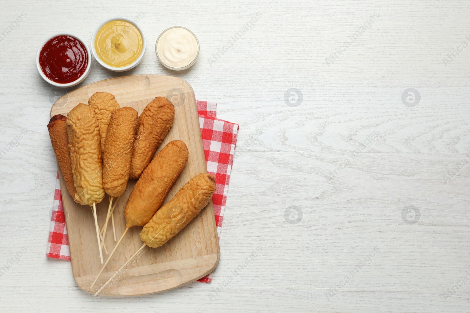 Photo of Delicious deep fried corn dogs with sauces on white wooden table, flat lay. Space for text