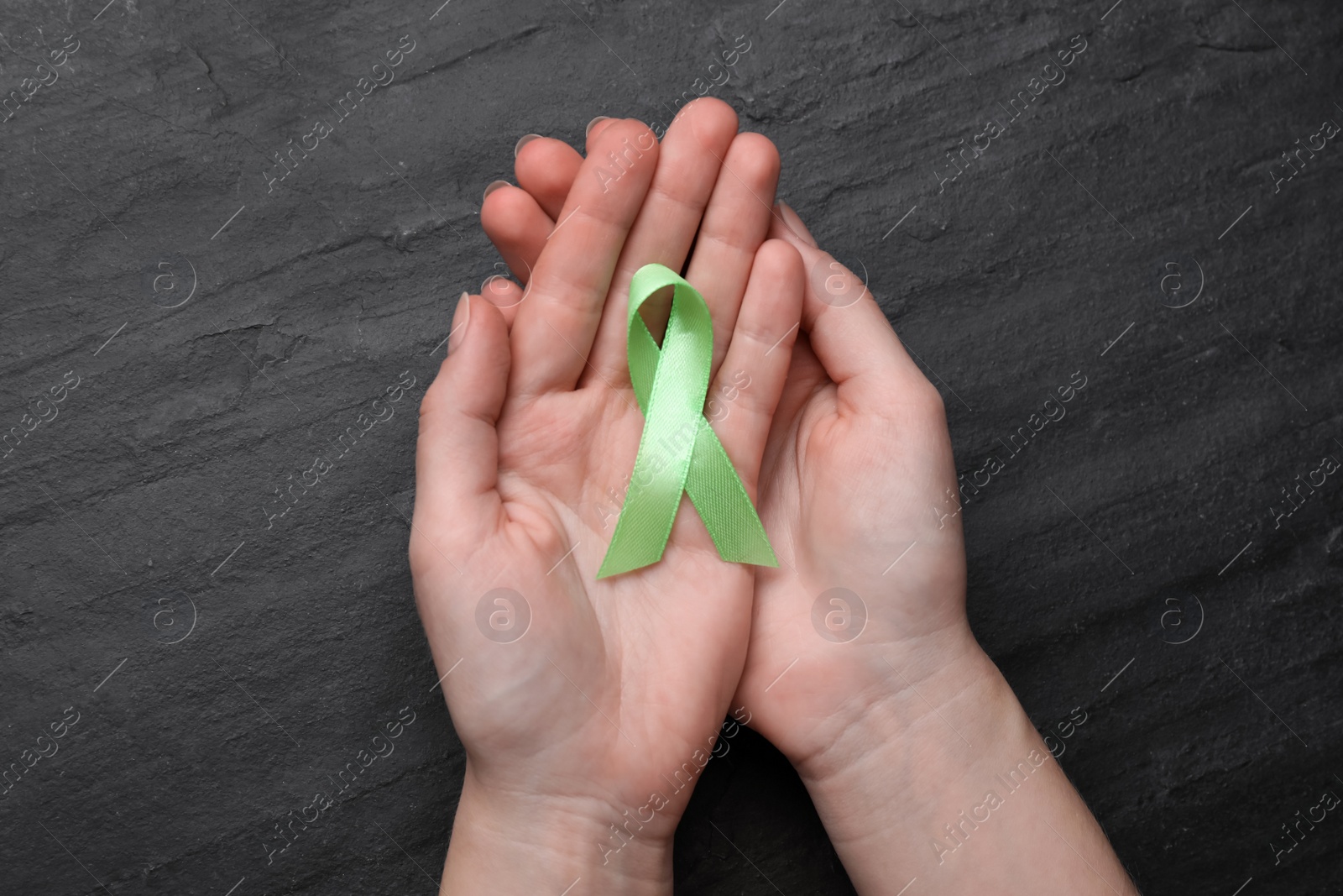 Photo of World Mental Health Day. Woman holding green ribbon on black background, top view