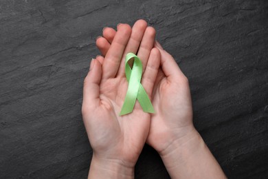 Photo of World Mental Health Day. Woman holding green ribbon on black background, top view