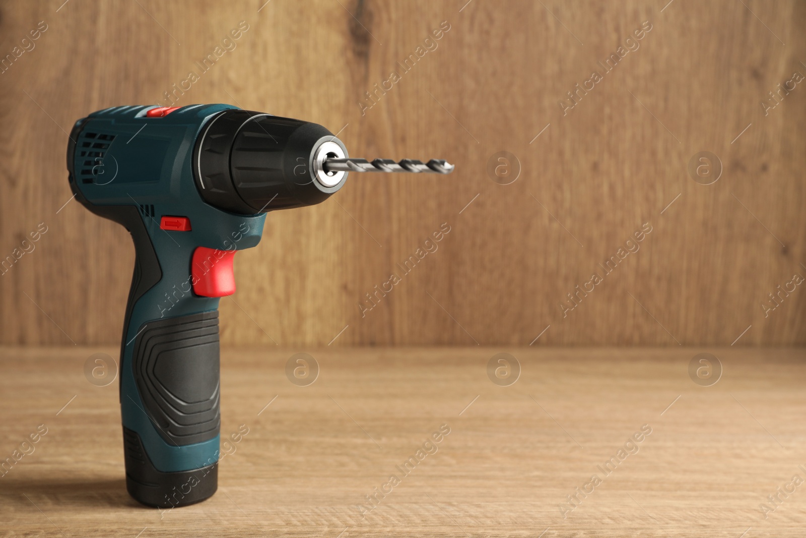 Photo of Modern electric power drill on wooden table, space for text