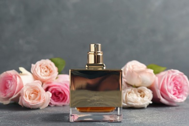 Photo of Bottle of perfume with beautiful roses on table