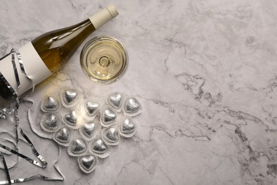 Heart made with delicious chocolate candies and champagne on white marble table, flat lay. Space for text