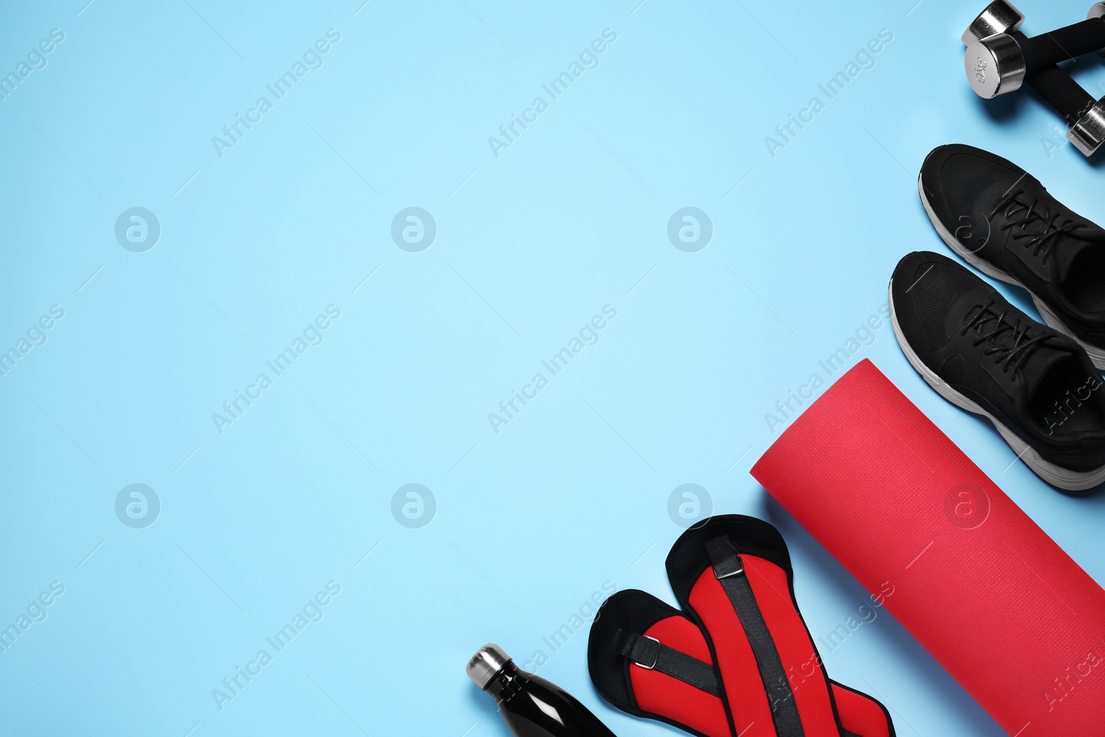 Photo of Exercise mat, dumbbells, bottle of water, weights and shoes on light blue background, flat lay. Space for text
