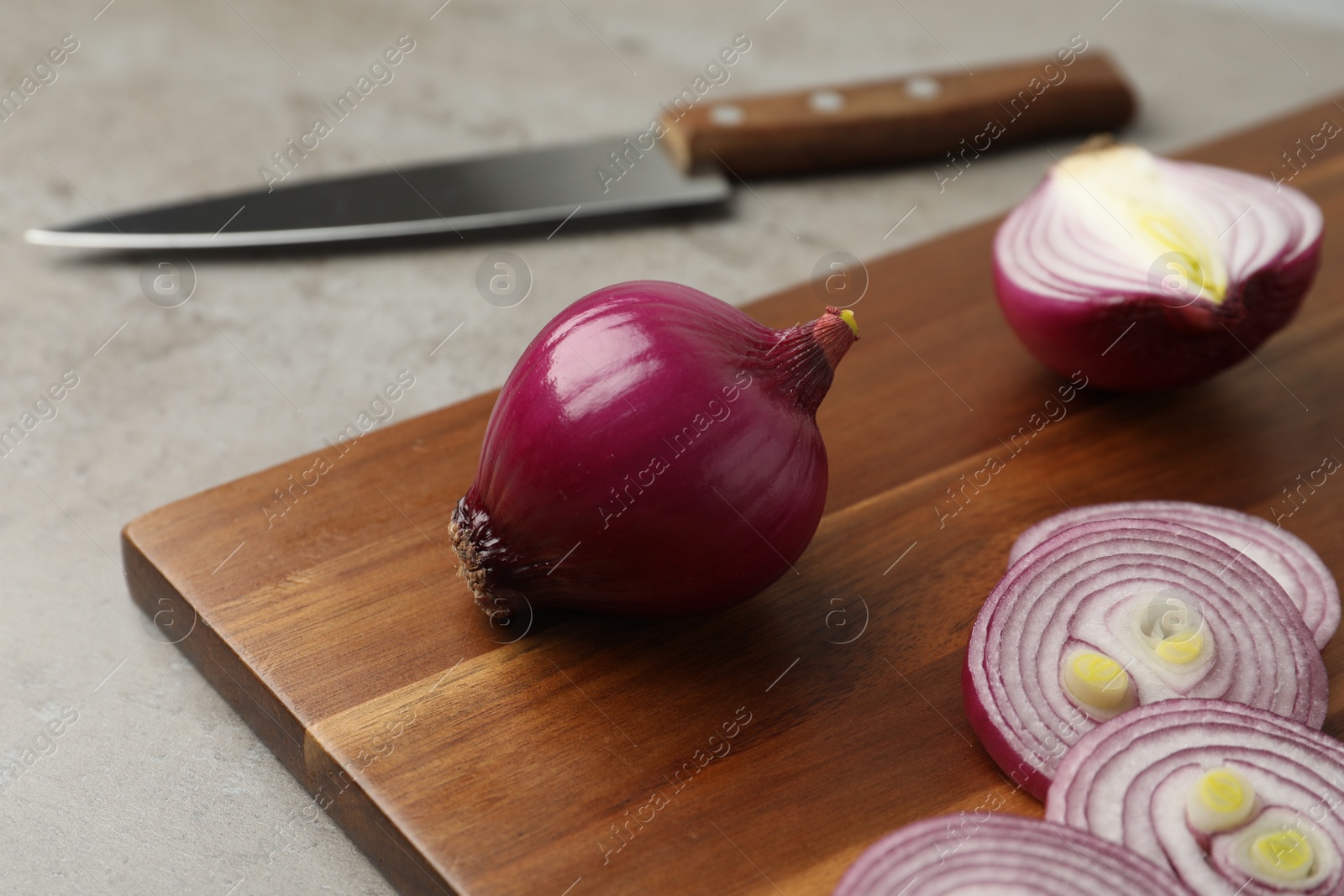 Photo of Red onion and wooden board on light grey table, closeup