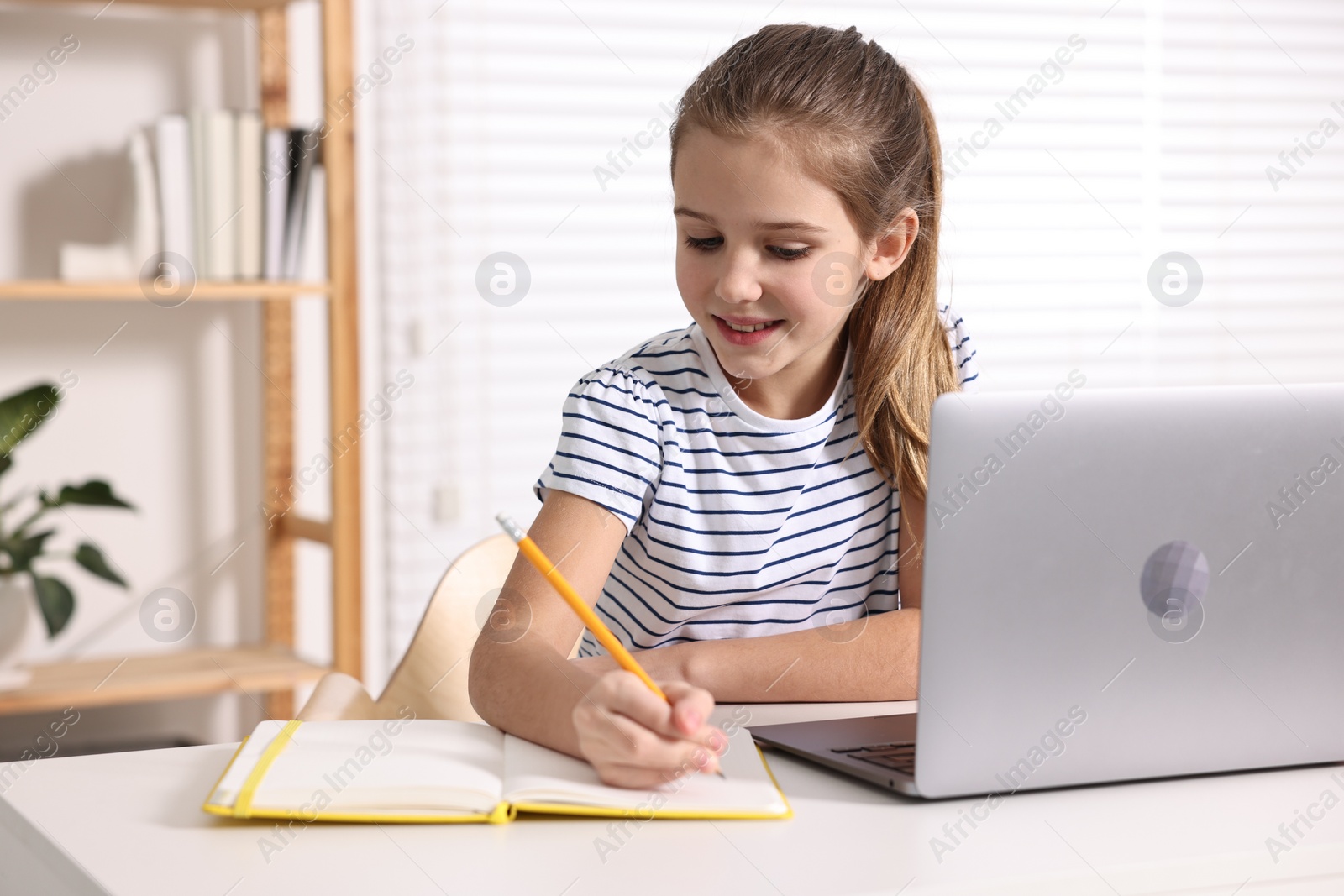 Photo of E-learning. Cute girl taking notes during online lesson at table indoors