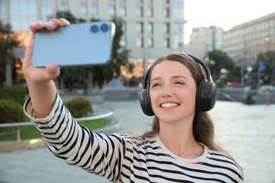 Smiling woman in headphones taking selfie on city street