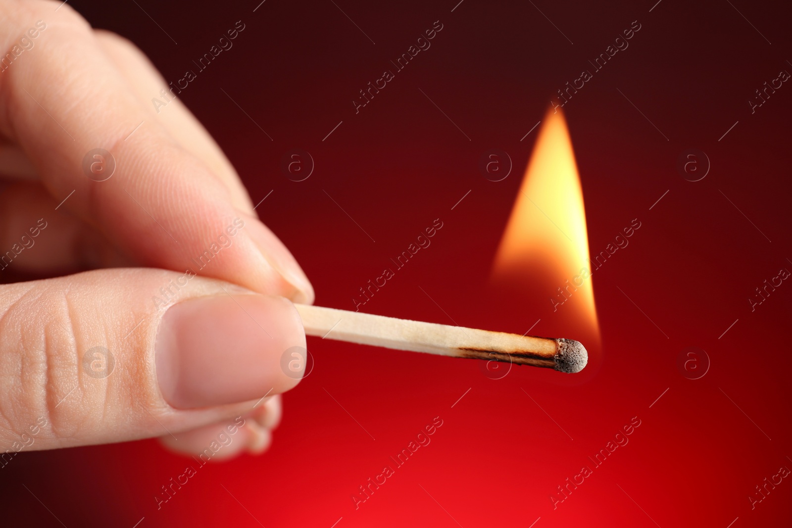 Photo of Woman holding burning match on color background, closeup