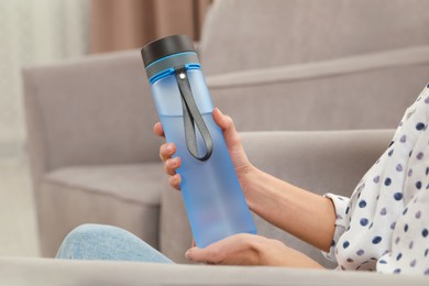 Woman with bottle of water at home, closeup