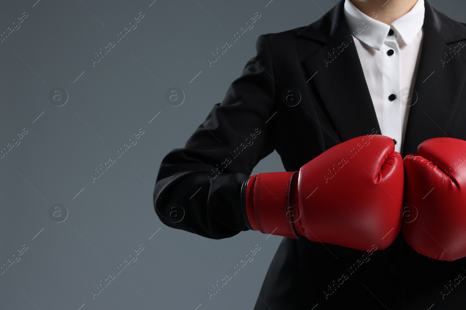 Photo of Businesswoman in suit wearing boxing gloves on grey background, closeup. Space for text